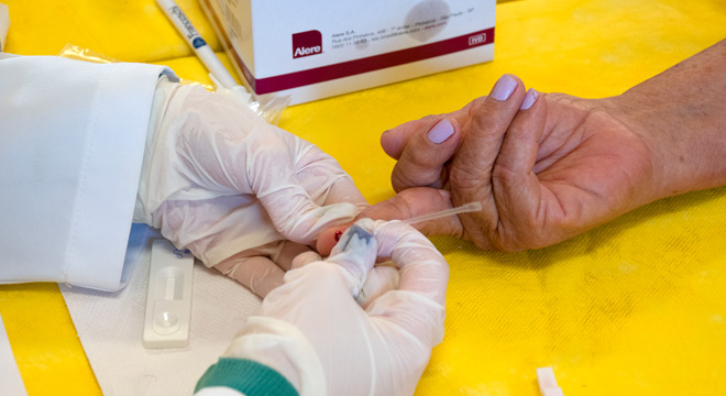 Só aparecem as mãos de profissional de saúde realizando teste de glicemia em paciente 