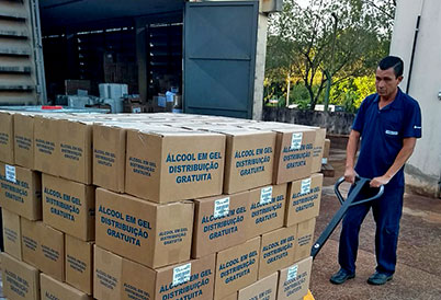 foto mostra homem puxando uma empilhadeira carregando caixas com os dizeres "álcool em gel para doação"
