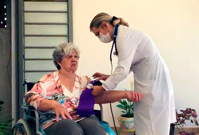 Uma profissional de saúde afere pressão arterial de uma idosa em cadeira de rodas 