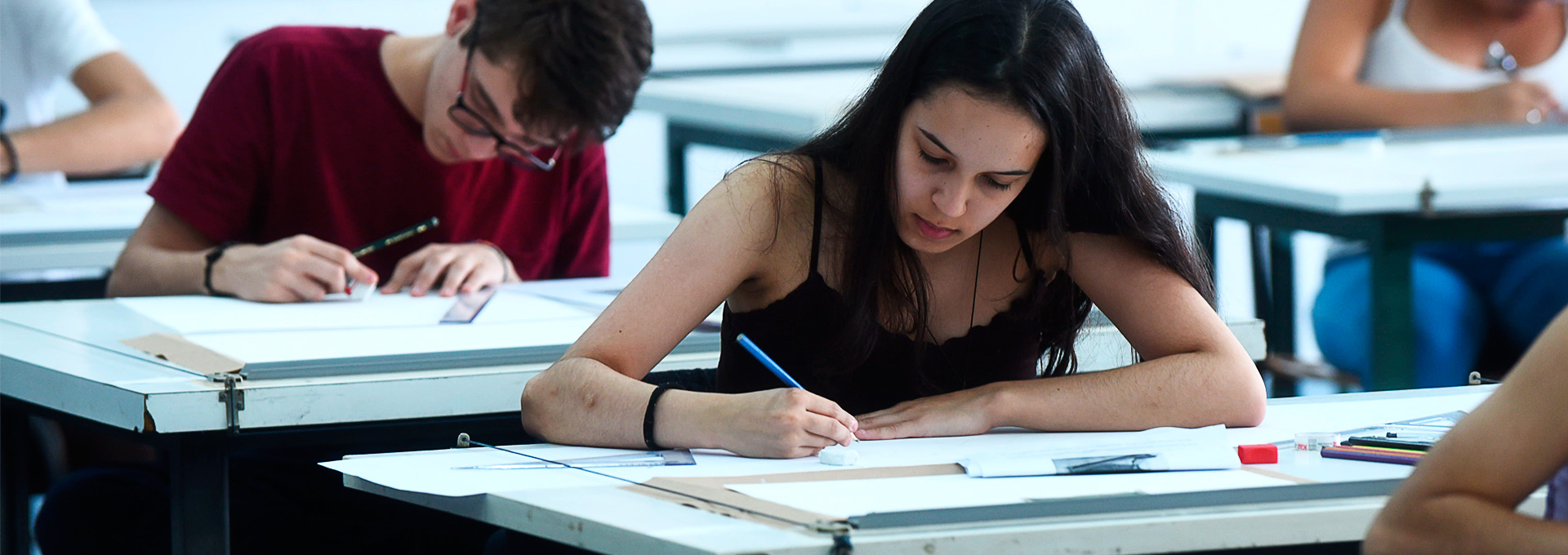 Dois estudantes em mesas fazendo a prova escrita do Vestibular