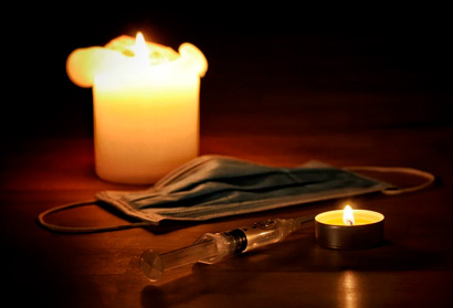 foto mostra velas acesas e uma máscara de proteção em uma mesa, simbolizando luto pelas mortes