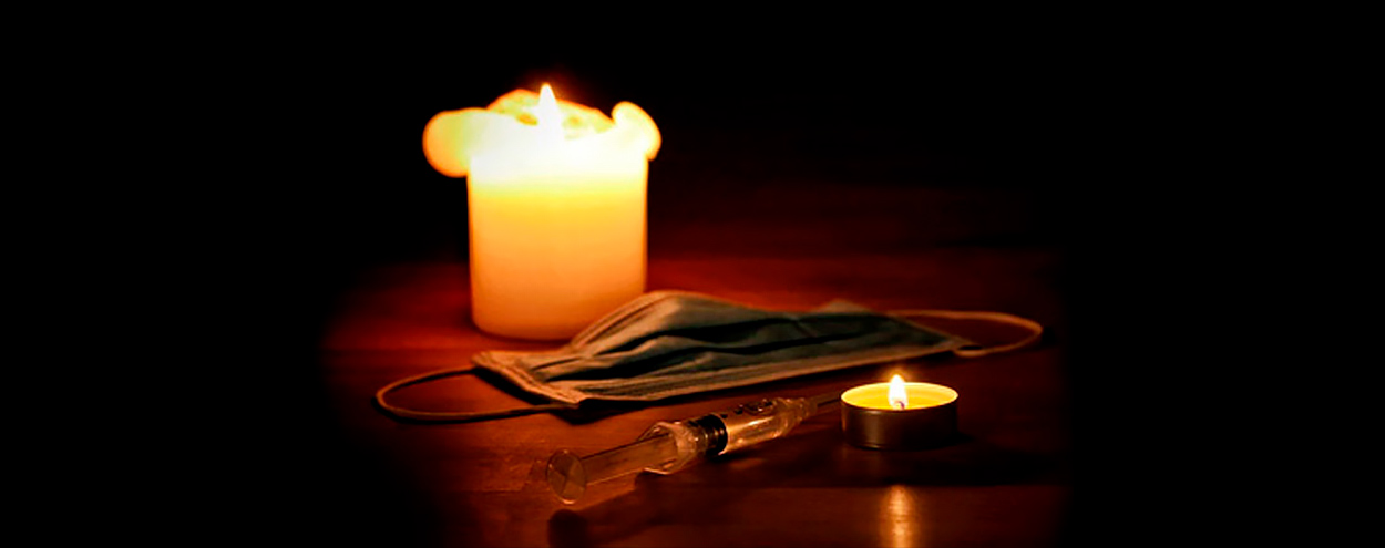 Imagem de uma vela acesa com uma máscara e seringa ao ao lado. Foto conceitual