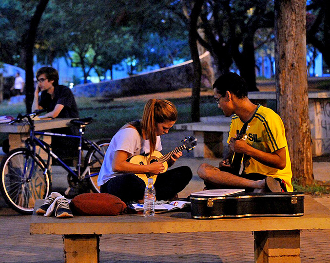 foto mostra alunos sentados em um banco da praça do ciclo básico tocando violão