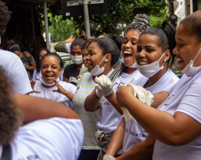 Cestas básicas e tablets já foram doados a ONGs de Florianópolis (SC) e do Rio de Janeiro (RJ). Atual etapa vai beneficiar grupo de mulheres de Natal (RN) foto mostra voluntárias do grupo rocinha resiste em uma ação. elas estão sorrindo e vestem a camiseta da ong