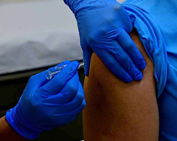 foto mostra uma mão com luvas aplicando uma vacina no braço de um paciente