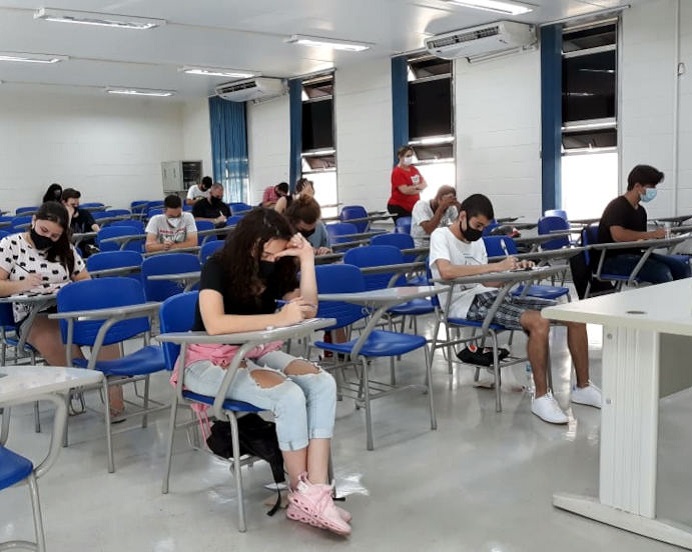 Segunda fase do vestibular é concluída sem intercorrências audiodescrição: fotografia colorida mostra candidatos, de máscara, realizando provas de vestibular em sala; as cadeiras são azuis e há poucos candidatos na sala, conforme protocolos de distanciamento social