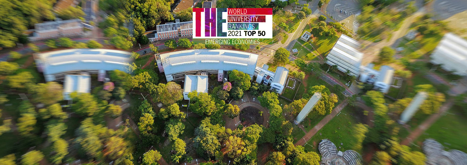 audiodescrição: imagem aérea com vista do ciclo básico da unicamp; logo colorida do ranking times higher education está aplicada sobre a fotografia