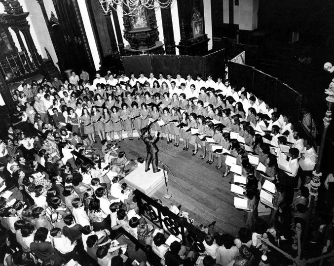 1º Concerto Oficial do Coral da Unicamp na Catedral Metropolitana de Campinas, 16 de novembro de 1971. Foto: Acervo Histórico do Arquivo Central da Unicamp audiodescrição: fotografia preto e branca de um coral em apresentação, no centro há um regente
