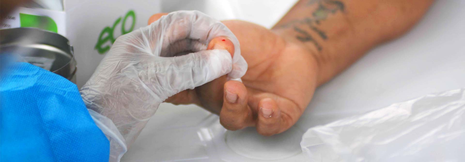 foto mostra mão de profissional de saúde, com luvas, coletando amostra de sangue do dedo de um paciente