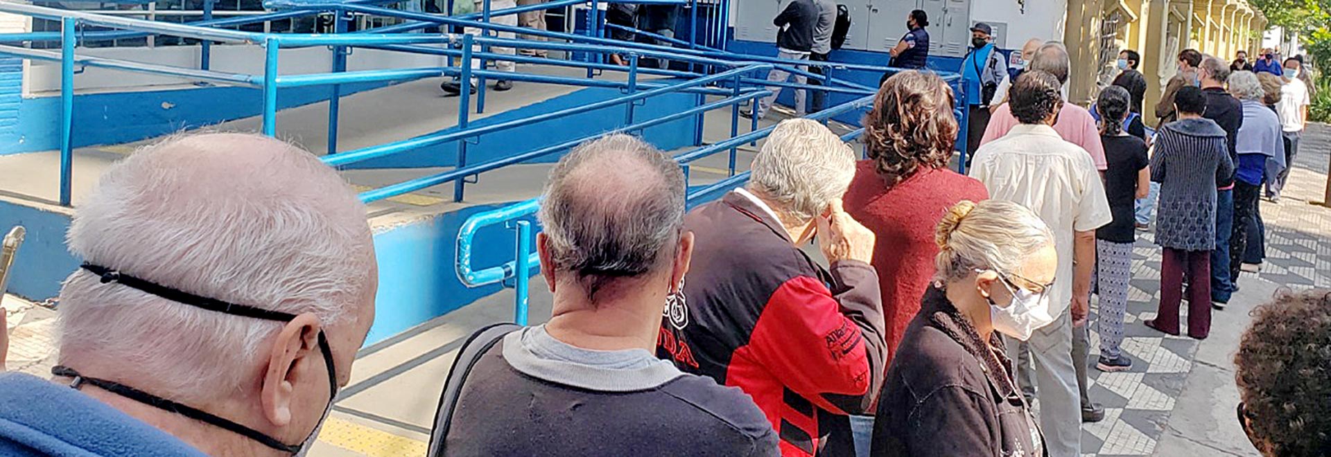 foto mostra idosos em uma fila em frente a unidade de saúde