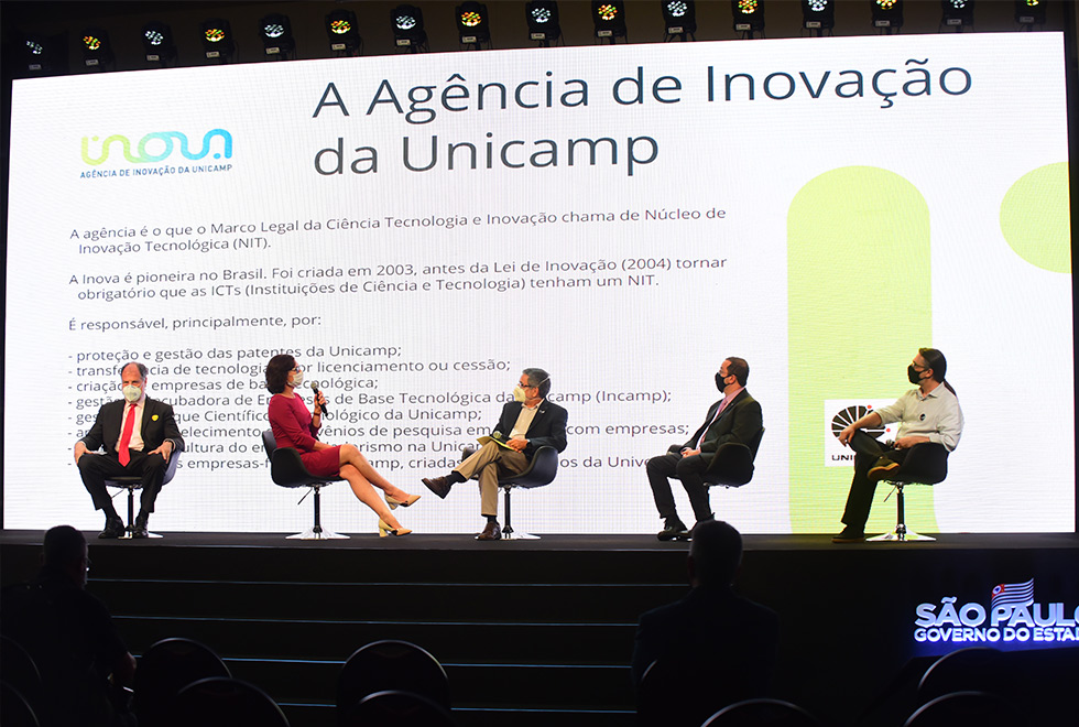 Inova Unicamp, HIDS e Coordenadoria de Georreferenciamento apresentaram seus trabalhos ao público (foto: Antonio Scarpinetti) foto mostra professores da unicamp sentados em cadeiras no palco com o telão ao fundo