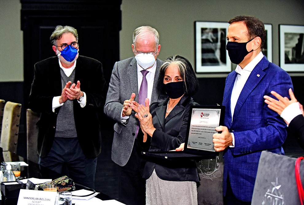 Universidades estaduais recebem R$ 1 bilhão em repasse do Governo de São Paulo foto mostra joão dória mostrando placa de homenagem que recebeu de vanderlan bolzani, presidente da aciesp