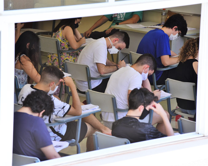 audiodescrição: fotografia colorida de estudantes realizando a prova do vestibular em uma sala; a foto foi feita fora da sala e é possível ver os candidatos através de uma janela