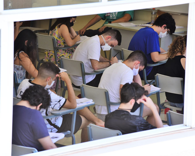Candidatos realizam a primeira fase do vestibular neste domingo (7) audiodescrição: fotografia colorida de estudantes realizando a prova do vestibular em uma sala; a foto foi feita fora da sala e é possível ver os candidatos através de uma janela