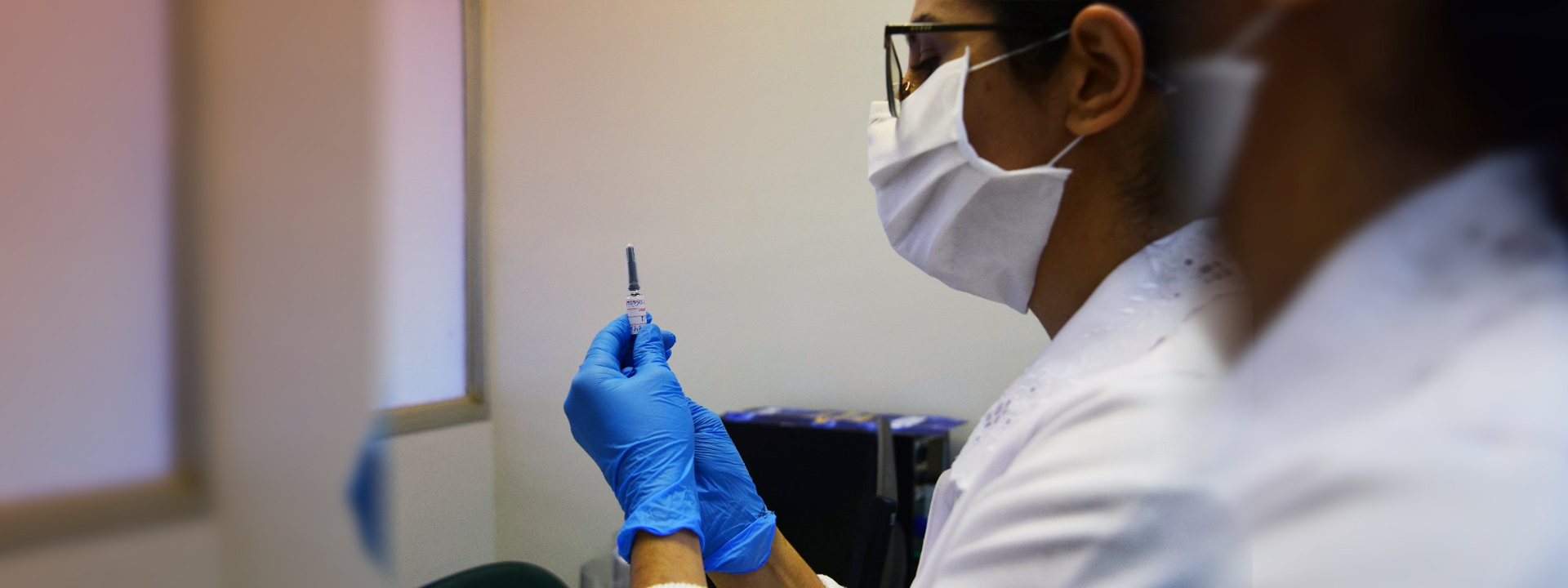 foto mostra uma profisisonal de saúde, com máscara, segurando uma seringa com dose de vacina