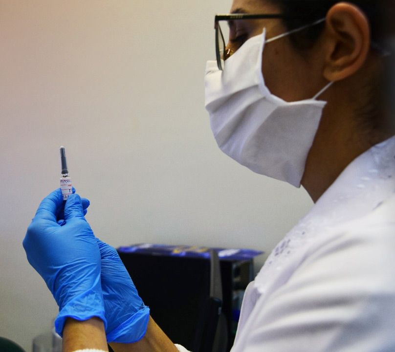 foto mostra uma profisisonal de saúde, com máscara, segurando uma seringa com dose de vacina