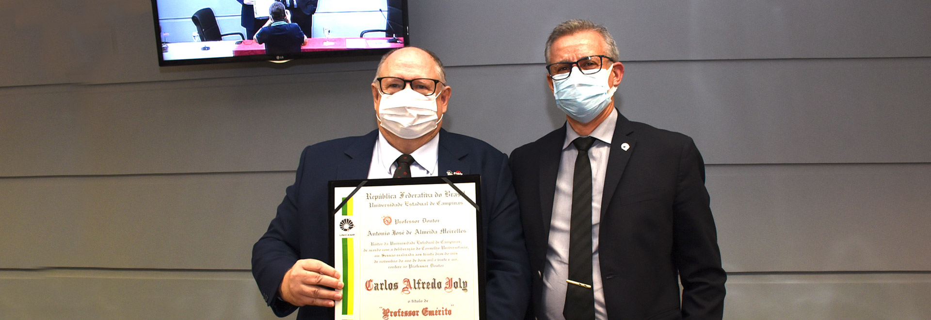 "Não basta preservar o que restou, precisamos restaurar". Docente foi pioneiro da ecofisiologia vegetal moderna no país foto mostra carlos joly segurando o diploma de professor emérito e o reitor antonio meirelles
