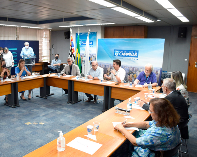 foto mostra pessoas sentadas em mesas, no formato de U, em uma sala da prefeitura de campinas