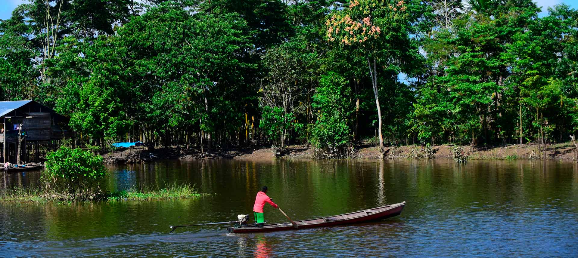 audiodescrição: um lago ao lado da floresta amazônica. Um barco com pescadores.