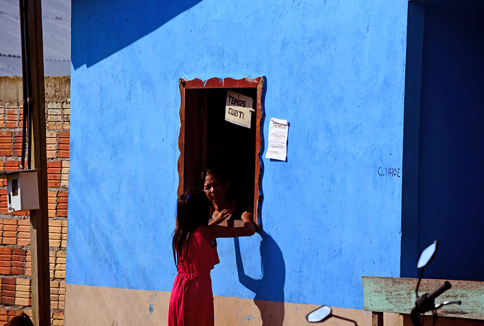audiodescrição: fotografia colorida de pessoas na janela em casa da comunidade indígena