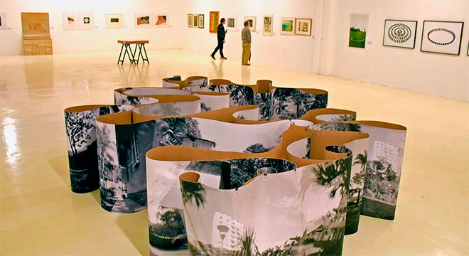 Fotografia de uma das obras da exposição que fica no chão e tem formato de uma superfície em espiral com fotos impressas e em preto e branco