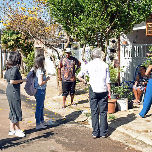 Imagem mostra grupo de pessoas conversando na rua, em frente à uma casa.