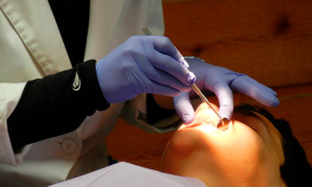 Foto mostra dentista examinando a boca de um paciente.