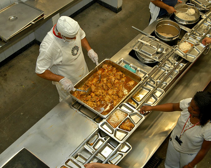 Foto mostrando funcionário servindo alimento em restaurante industrial