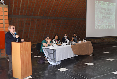 Audiodescrição: imagem colorida, a esquerda o pró-reitor de Pesquisa, João Romano, falando ao microfone, a ao centro está uma mesa com quatro participantes do evento (Foto: Antonio Scarpinetti)