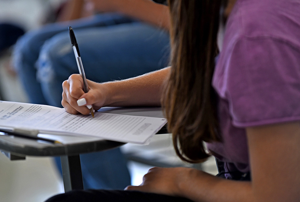 A segunda fase acontecerá, pelo segundo ano consecutivo, no mês de dezembro Audiodescrição (AD). Foto: Antonio Scarpinetti. Em ampla sala de aula, imagem em perspectiva e plano geral de cerca de 50 pessoas sentadas em carteiras escolares com braços, voltadas para a esquerda da foto, posicionadas uma ao lado da outra, formando 7 fileiras verticais. A maioria delas escreve com caneta ou lápis em folhas impressas das provas que estão sobre as carteiras, mantendo a cabeça levemente reclina para a frente. Quase todas vestem roupas casuais, como camiseta e bermuda. Imagem 1 de 1