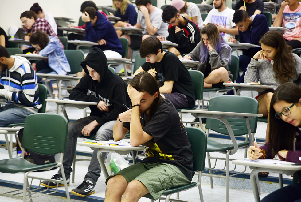 A galeria apresenta candidatos durante prova no Vestibular Unicamp 2018 e a entrevista coletiva com membros da Comissão Permanente para os Vestibulares (Comvest). Para acessá-la, tecle enter. Audiodescrição: Em ampla sala de aula, cerca de vinte pessoas, entre homens e mulheres, sentados em carteiras escolares de braço, realizam prova, sendo que a maioria mantém a cabeça abaixada, concentrada na prova. As carteiras estão dispostas uma ao lado da outra, formando várias fileiras em desnível. Imagem 1 de 10.