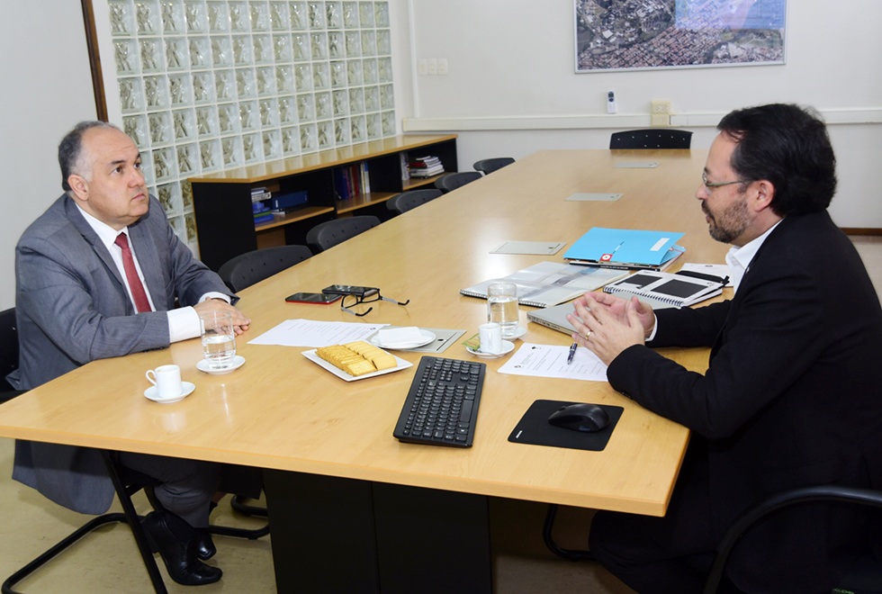 Reunião entre o secretário adjunto de Cultura do Estado de São Paulo, Romildo Campello (à esq.), e o pró-reitor de Extensão e Assuntos Comunitários Fernando Hashimoto, realizada na Unicamp A galeria traz a reunião entre o secretário adjunto de cultura do Estado de São Paulo e o pró-reitor de Extensão e Assuntos Comunitários da Unicamp. Para acessá-la, tecle enter. Audiodescrição: Em sala de reuniões, dois homens sentados em cadeiras, um de frente para o outro, sendo que entre eles há uma extensa mesa retangular de madeira. Ambos vestem roupa social, como blazer e gravata. Na sala, há uma parede de tijolinhos de vidro e um mapa com foto de imagem aérea da Unicamp na parede. Imagem 1 de 3.