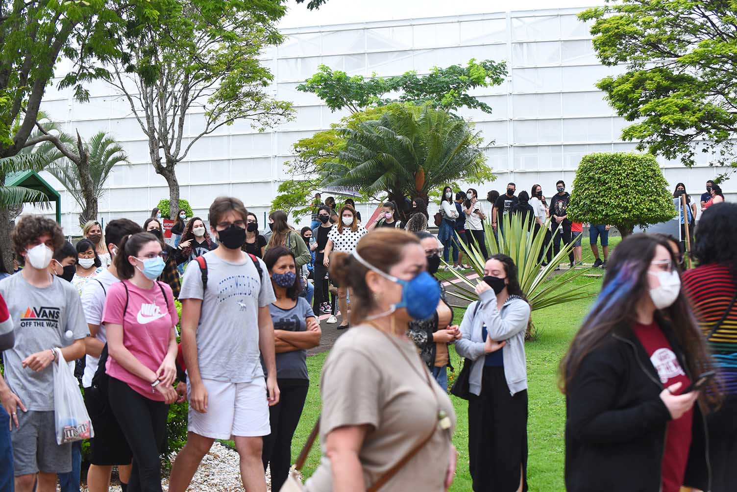 Chegada de candidatos para provas da segunda fase do Vestibular Unicamp 2022, na PUC-Campinas Audiodescrição: Em área externa, imagem de corpo inteiro de cerca de 40 pessoas que caminham em fila, do fundo da imagem para a frente, em trecho com curva. Há ampla área gramada e árvores no entorno deles. Ao fundo, parte de uma edificação. Todos usam máscaras e vestem roupas casuais como bermuda e camiseta. O dia está nublado. Imagem 9 de 20.