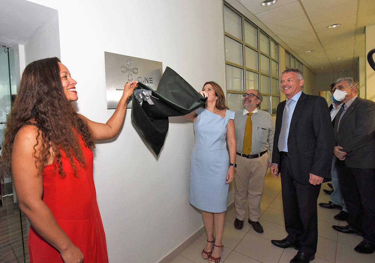 Descerramento de placa inaugural do Centro de Inovações de Novas Tecnologias (CINE) na Unicamp Audiodescrição: Em área interna, imagem de corpo inteiro de grupo com 6 pessoas em pé, que descerram placa inaugural retangular de inox, afixada em uma parede branca, à esquerda na imagem, onde se lê CINE, ao lado de um logotipo. Há uma mulher à esquerda, sorrindo, que puxa um tecido preto juntamente com outra mulher, à direita na imagem, de modo a descobrir a placa. Às costas dela, outras pessoas observam, sorrindo. Todos vestem roupas sociais. Imagem 1 de 18.