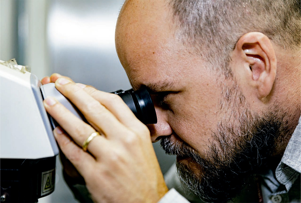 Foto mostra um homem olhando em um microscópio.
