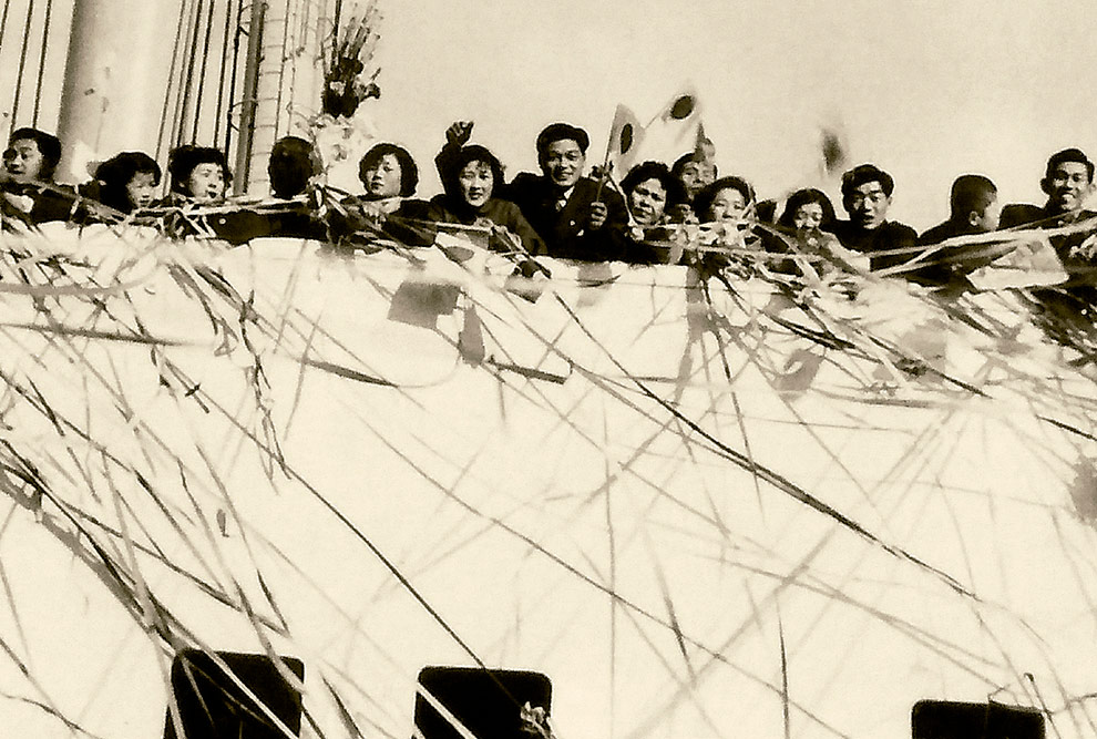Foto em preto e branco de pessoas na beira do convés de um navio.