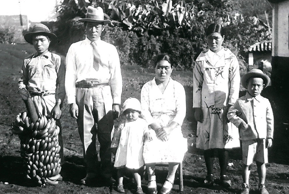 Foto em preto e branco de uma família de japoneses em frente a uma casa.