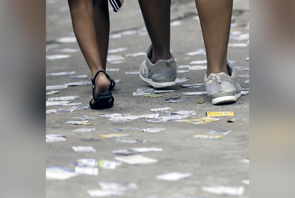 Pedestres passam em calçada com folhetos de propaganda política no primeiro turno das eleições de 2023, no bairro da Tijuca, no Rio de Janeiro