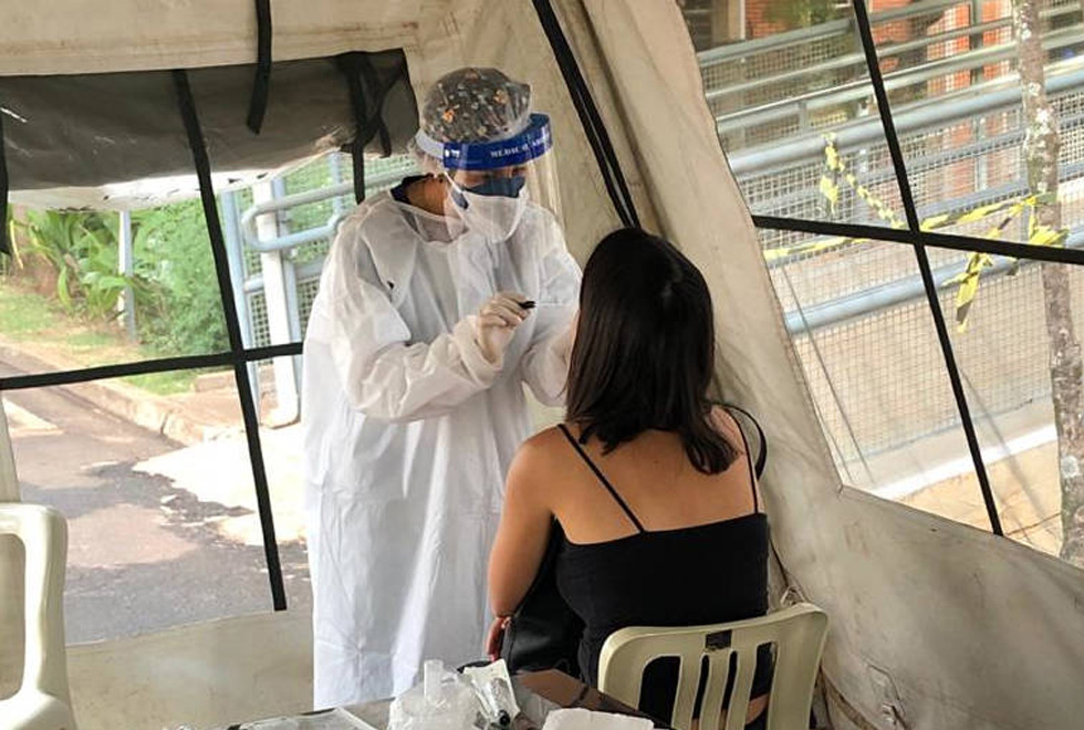 foto mostra enfermeira, com roupas de segurança, fazendo teste do tipo swab em uma paciente