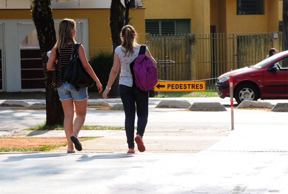 foto mostra duas estudantes caminhando, elas são enquadradas de costas. usam roupas casuais e levam mochilas