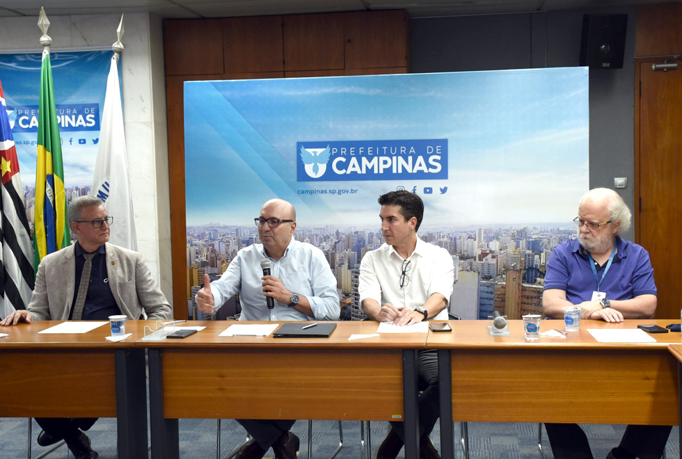 foto mostra pessoas sentadas em mesas, no formato de U, em uma sala da prefeitura de campinas