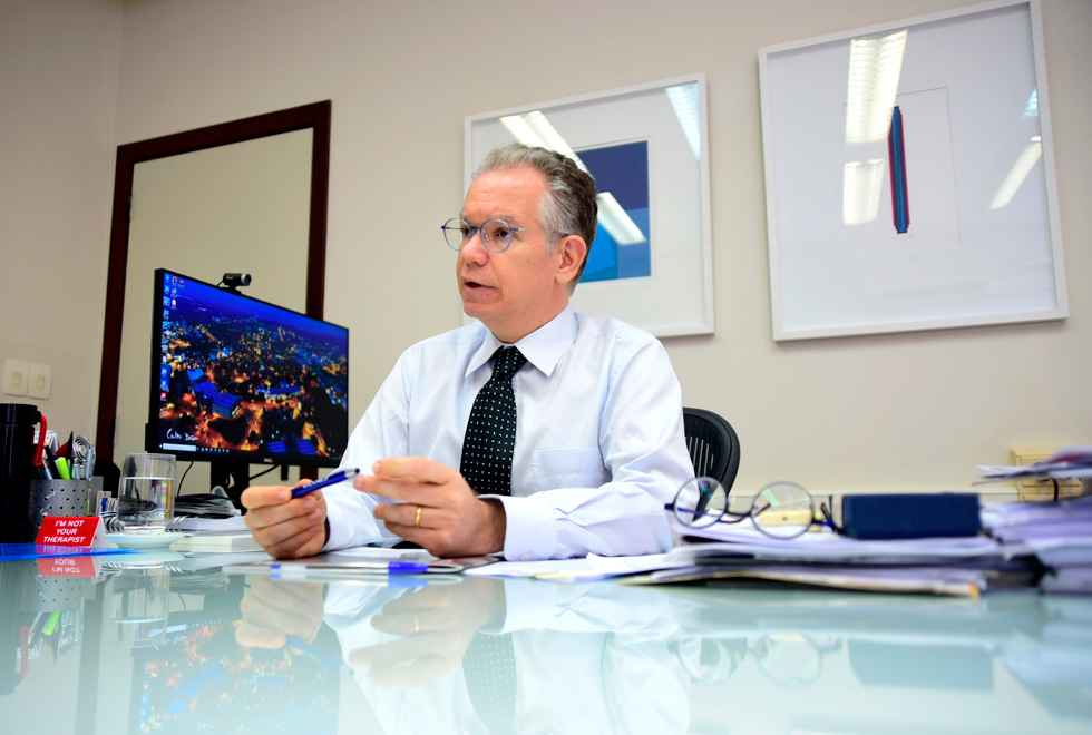 foto mostra o reitor da unicamp, marcelo knobel, sentado à mesa. ele veste camisa com gravata e usa óculos