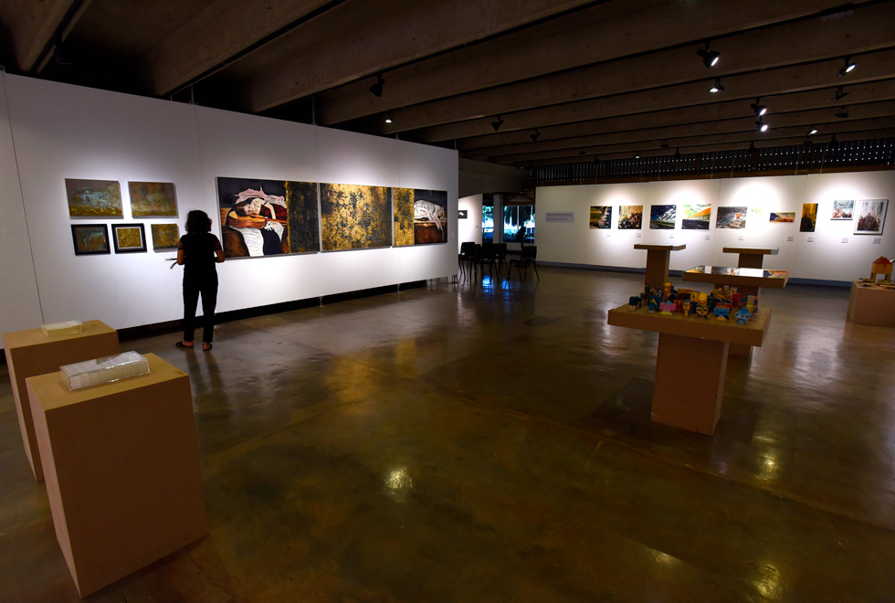 Audiodescrição: fotografia colorida em plano aberto mostra exposição dentro de Galeria de Arte da Unicamp; em cada parede há um conjunto de obras