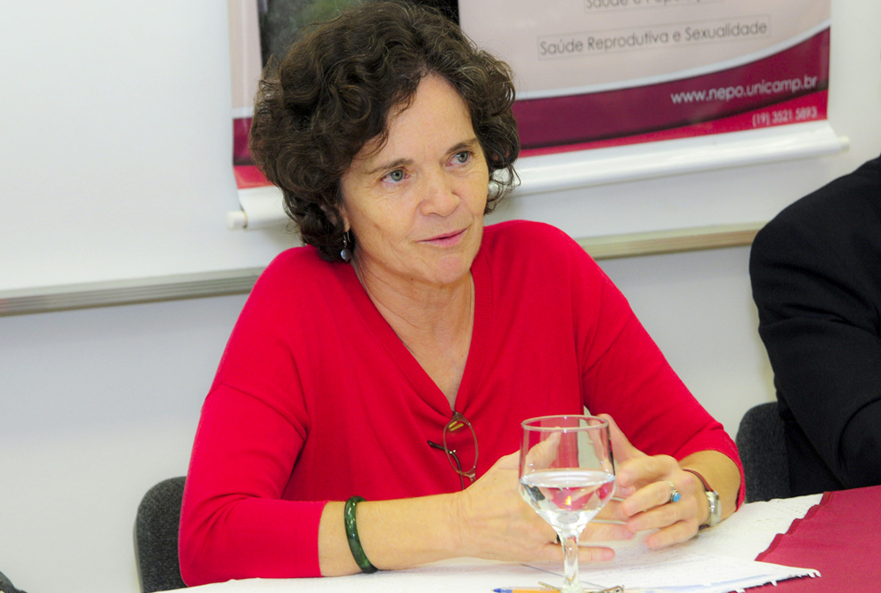audiodescrição: fotografia colorida da professora marta azevedo; ela veste vermelho e está sentada atrás de uma mesa de auditório