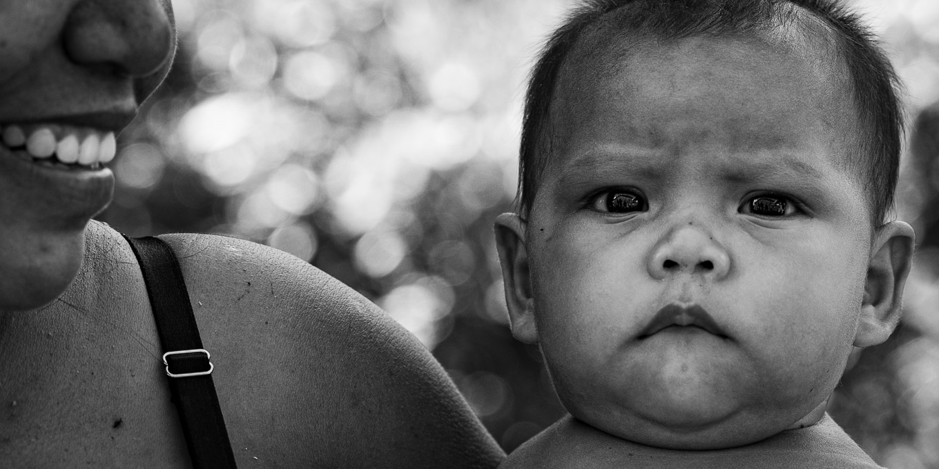 áudio descrição: fotografia em preto e branco de bebê yanomami no colo de sua mãe.