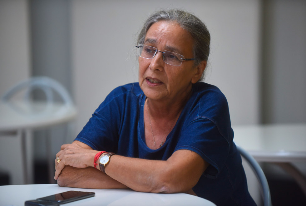 audiodescrição: fotografia colorida. professora do instituto de geociências, leda Gitahy, durante entrevista. ela está falando, com os braços cruzados, e usa blusa azul eóculos. 