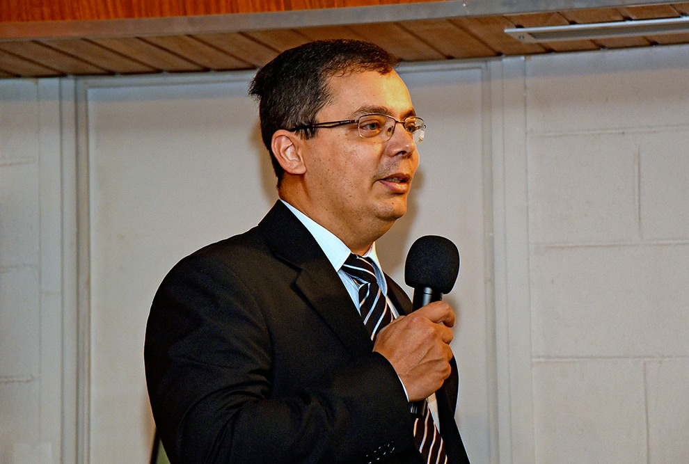 foto mostra o professor sando rigo falando ao microfone. ele veste terno
