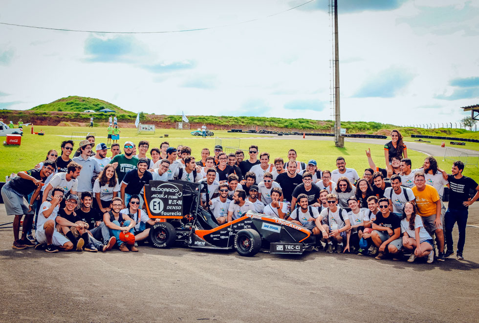 audiodescrição: fotografia colorida da equipe E-Racing junto a carro desenvolvido por eles
