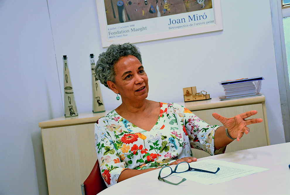 foto mostra professora silvia santiago. ela está sentada à mesa, com um óculos em sua frente, gesticulando