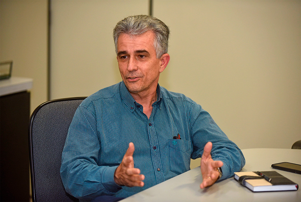 audiodescrição; fotografia colorida do diretor do instituto de química, marco aurélio zezzi. na foto, ele está gesticulando, sentado em frente a uma mesa, enquanto concede entrevista